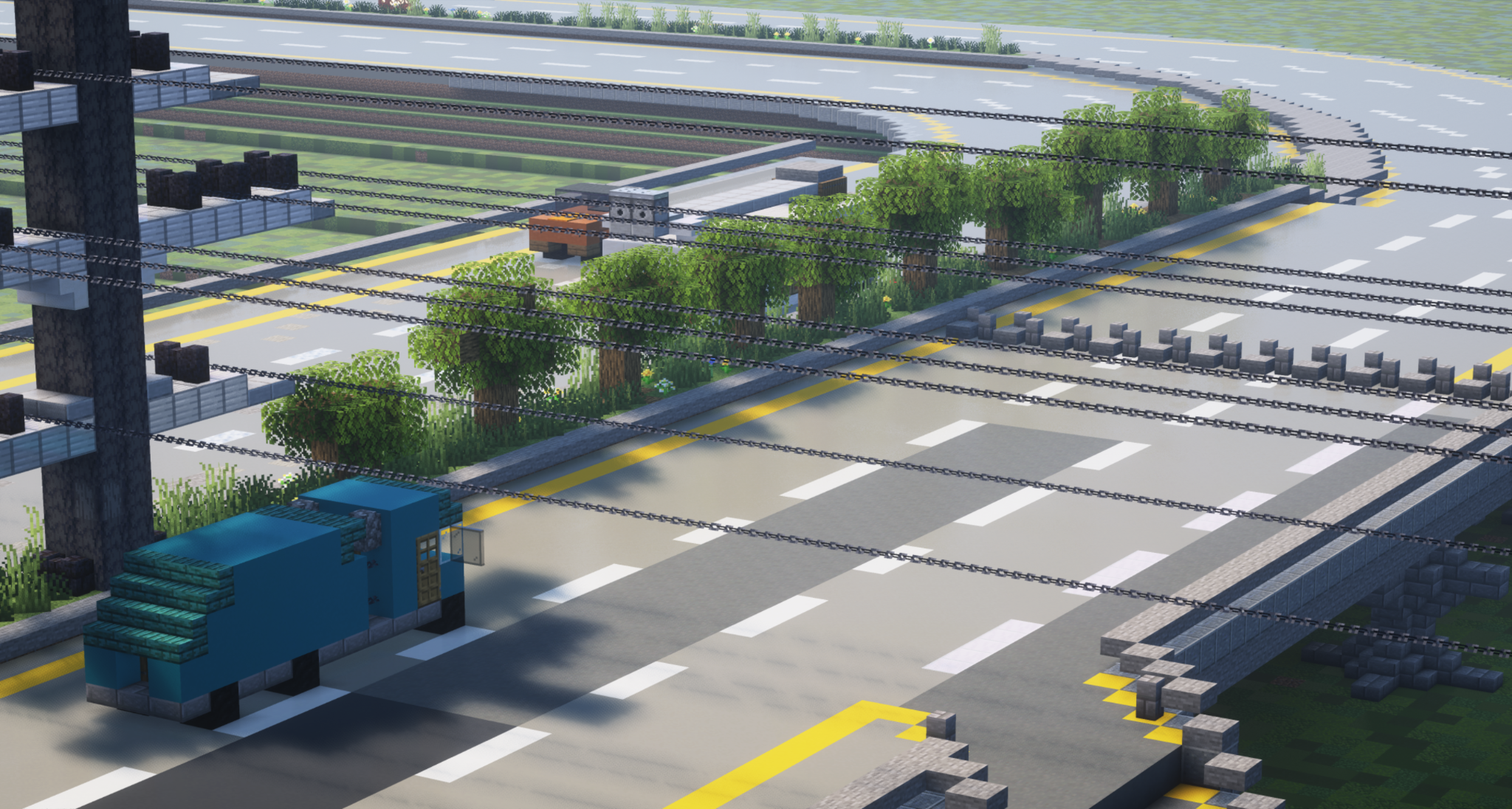 The picture shows a country road lined with trees and running under a high-voltage power line. A blue truck is driving on the road in the viewer's line of sight. A yellow car and a building can be seen in the background. The road is gray and has yellow lines on the sides marking the lanes.